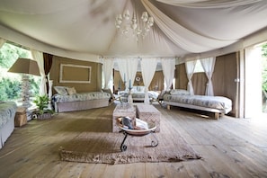 A tented accommodation with a central seating area, multiple beds, and a chandelier.