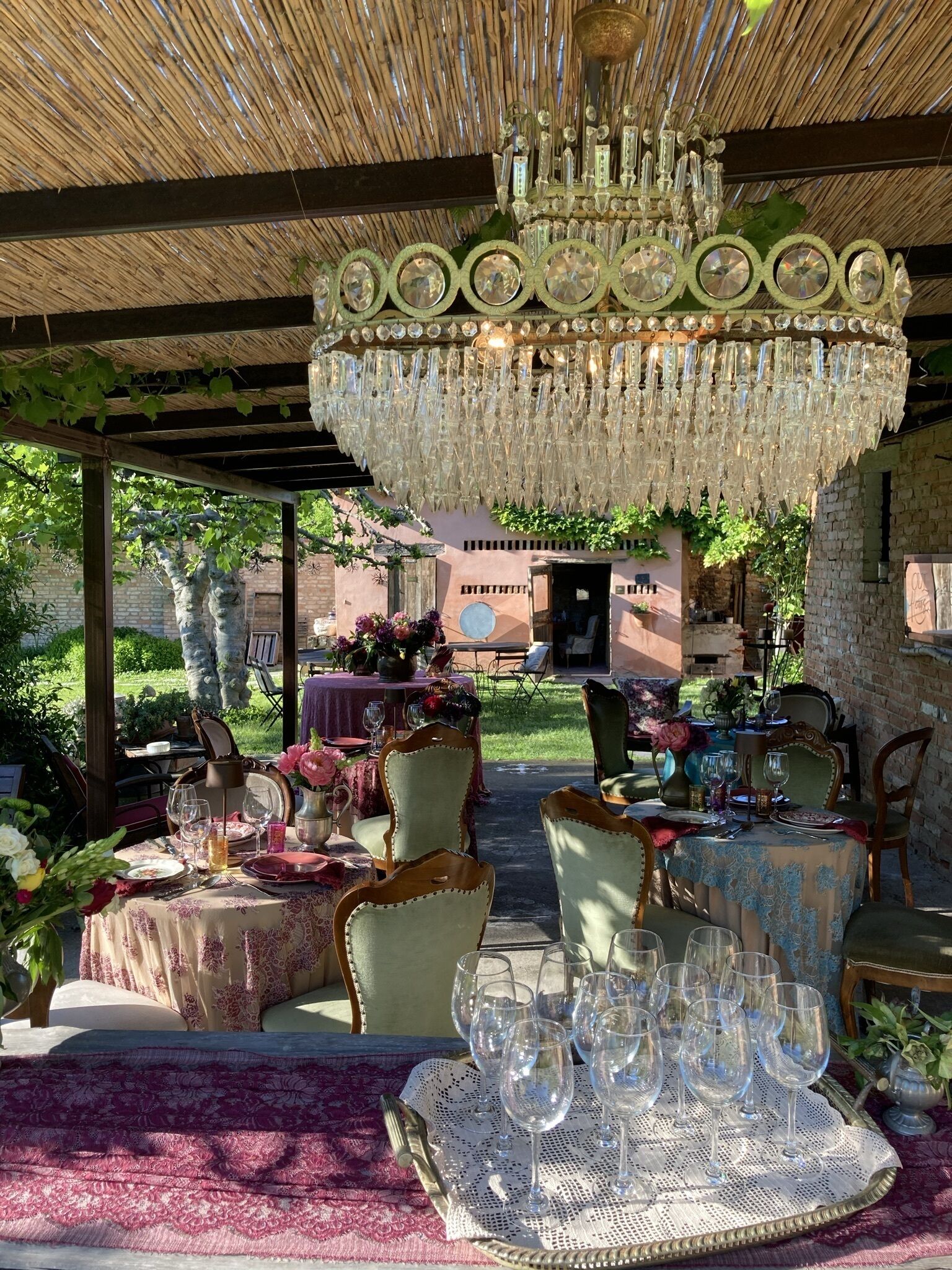 Un espacio al aire libre para comer con un candelabro grande, mesas dispuestas con copas de vino y sillas.