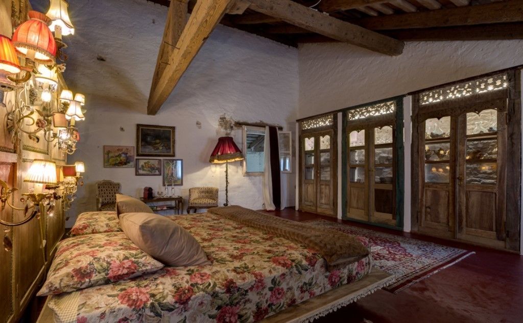 A bedroom with a large bed, wooden beams, a chandelier, and a window with decorative glass panes.