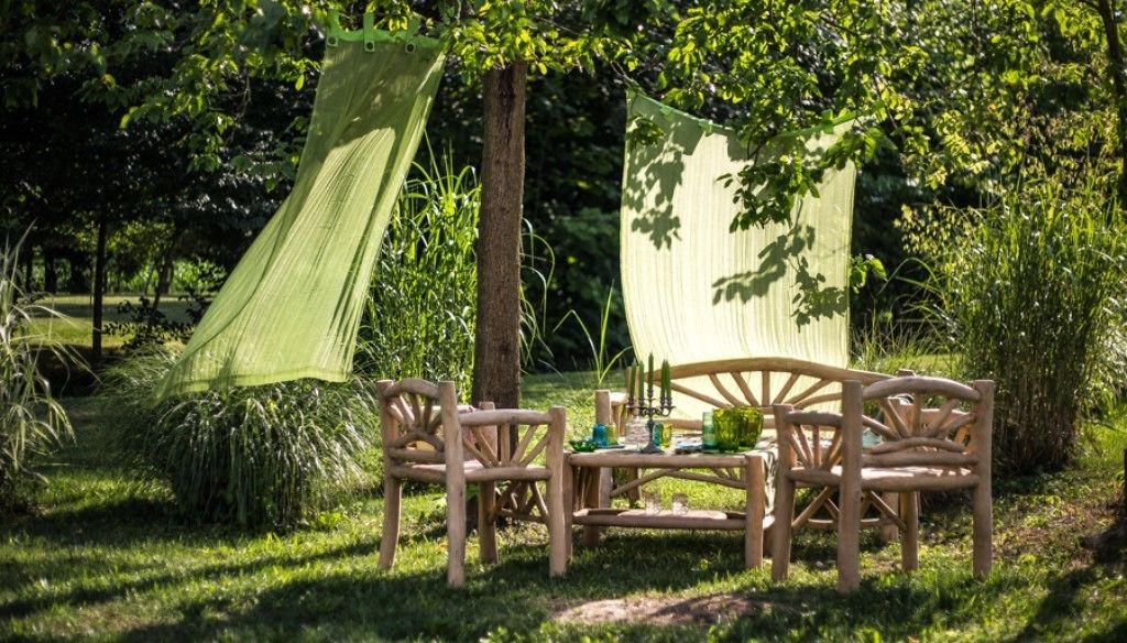 Une table et des chaises en bois, installées à l’extérieur, dans un espace herbeux, avec un hamac et une zone ombragée.