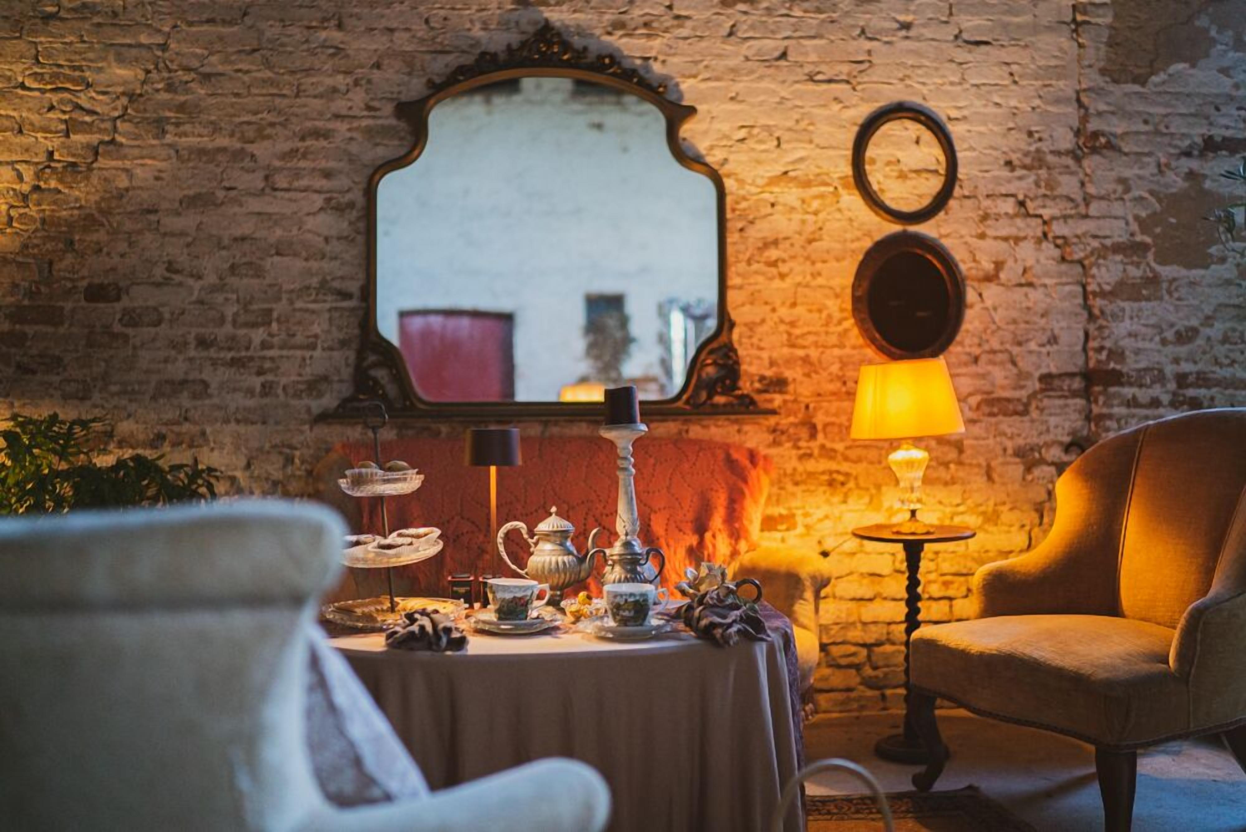A cozy room with a brick wall, a round mirror, a table set with tea and teapots, and a chair.