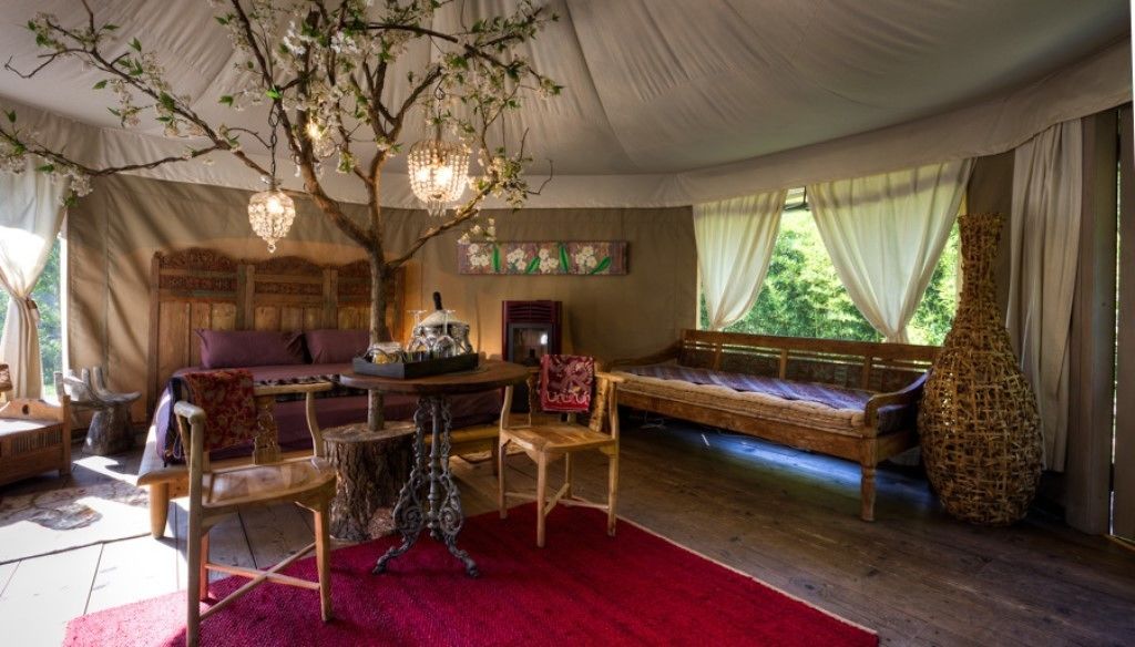 A tented room with a wooden bed, a table with chairs, a chandelier, and a large window with curtains.