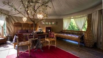 A tented room with a wooden bed, a table with chairs, a chandelier, and a large window with curtains.