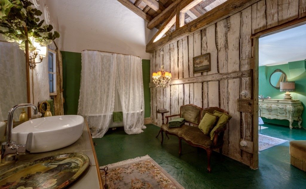 A rustic bathroom with a white sink, wooden walls, a green floor, a chair, and a chandelier.