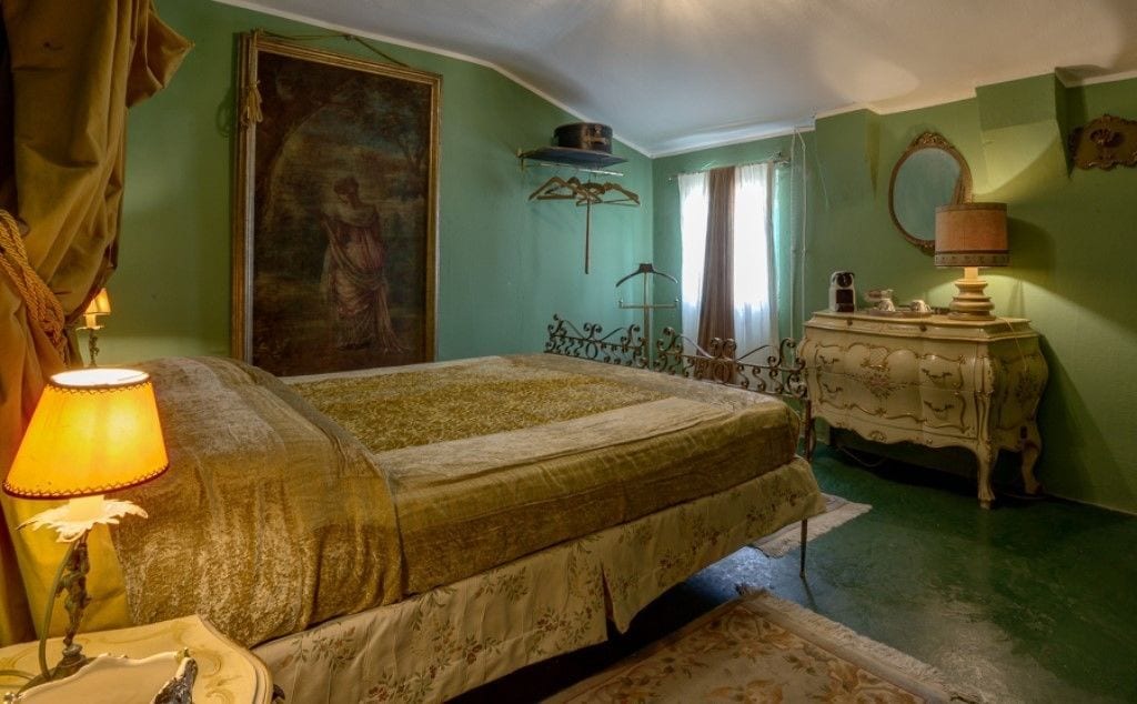 A bedroom with a bed, a dresser, a mirror, and a painting on the wall.
