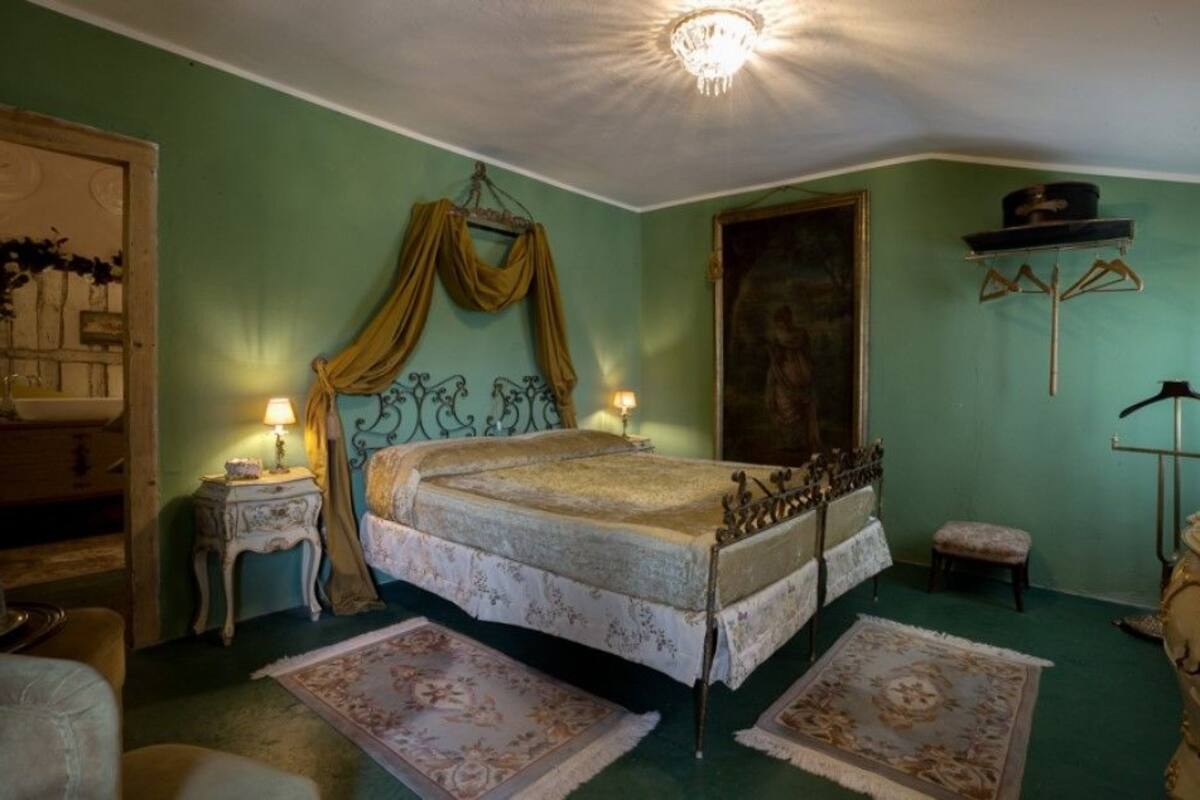 A bedroom with a bed, two bedside tables, a mirror, a painting, and a wardrobe.