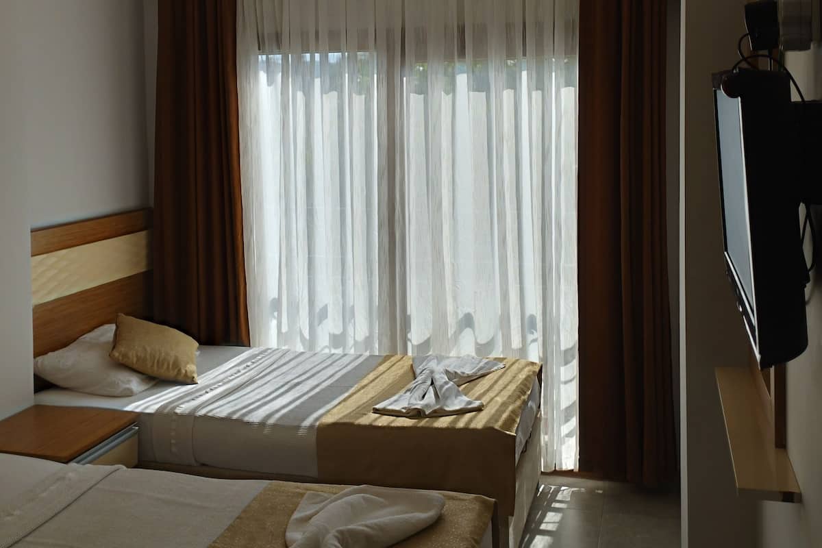 A hotel room with two beds, a flat-screen TV, and a large window with sheer curtains.