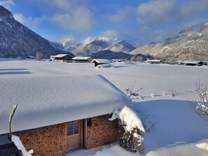 A snow-covered landscape with a rustic building, a clear sky, and mountains in the background.