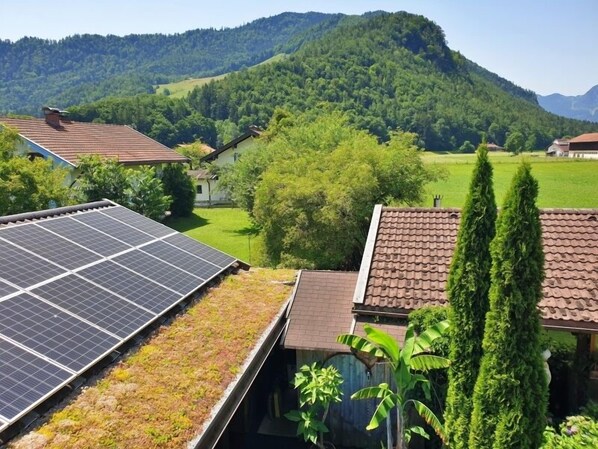 A house with a solar panel roof and a view of a green valley and mountains.
