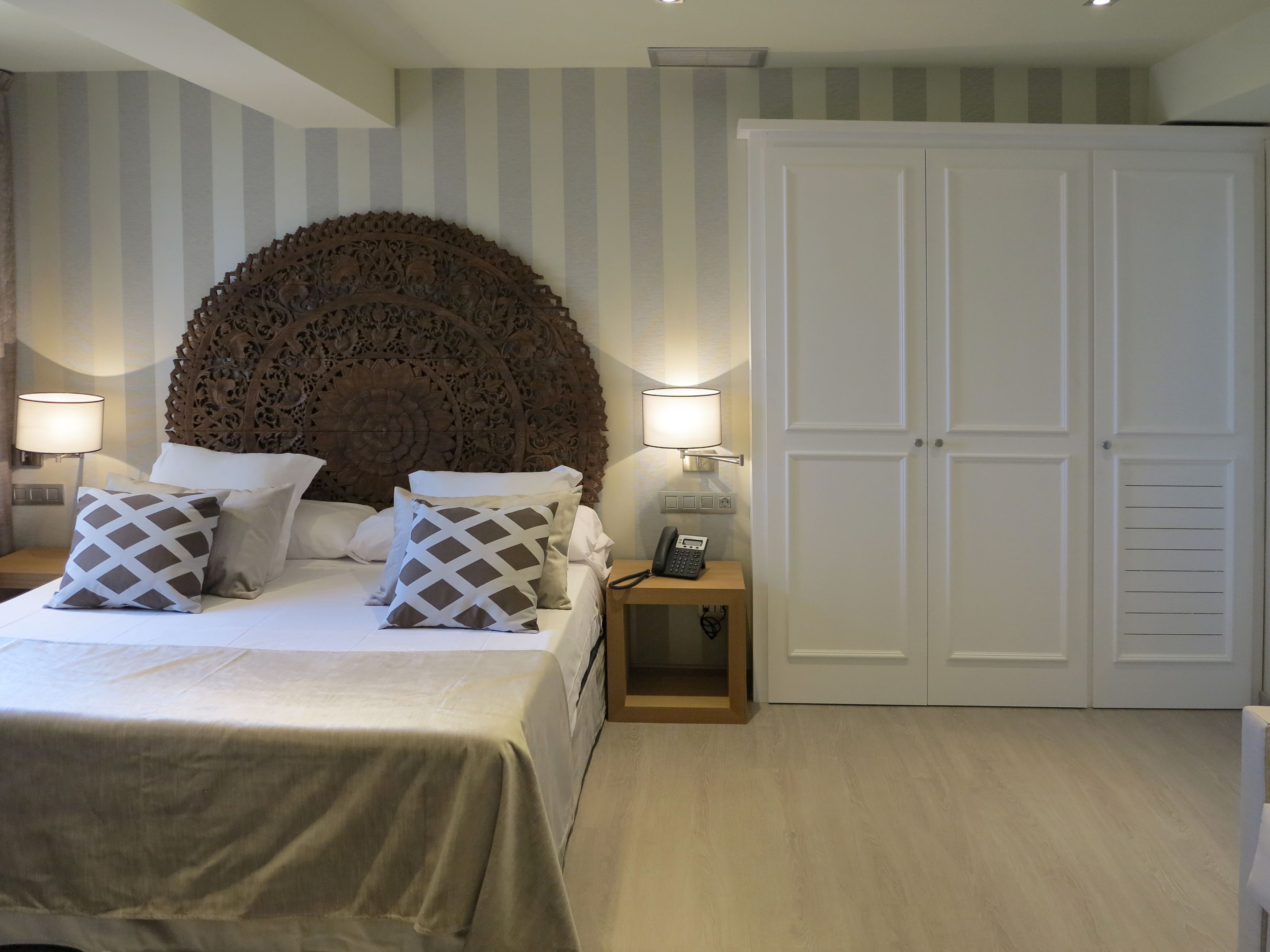 A hotel room with a large bed, two bedside lamps, a telephone, and a wardrobe.