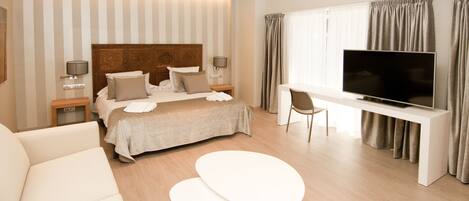 A modern hotel room with a large bed, a TV, a sofa, and a small table.