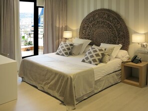 A neatly made bed with a decorative headboard, two bedside lamps, and a phone on a wooden nightstand. - Serennia Exclusive Rooms (Barcelona)