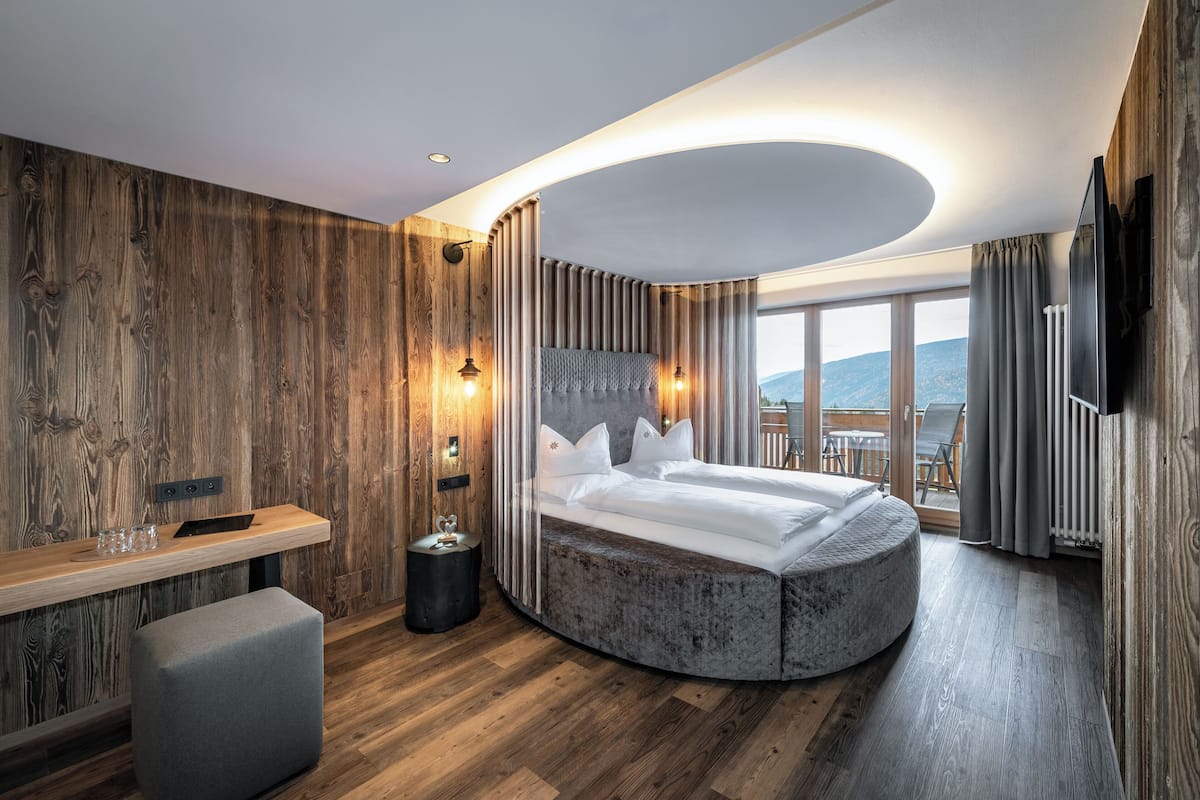 A modern bedroom with a curved bed, wooden walls, a bedside table, and a view of the outdoors.