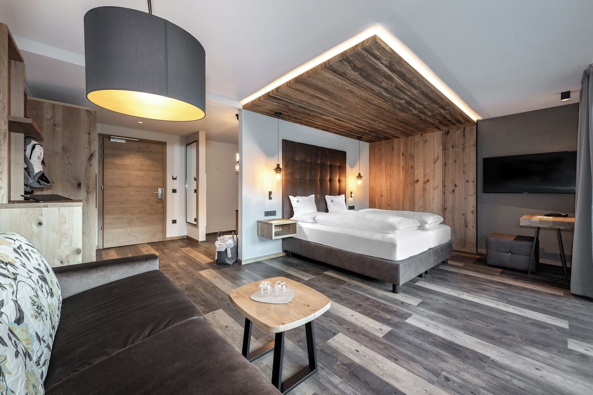A modern hotel room with a large bed, a wooden ceiling, a flat-screen TV, and a small table with glasses.