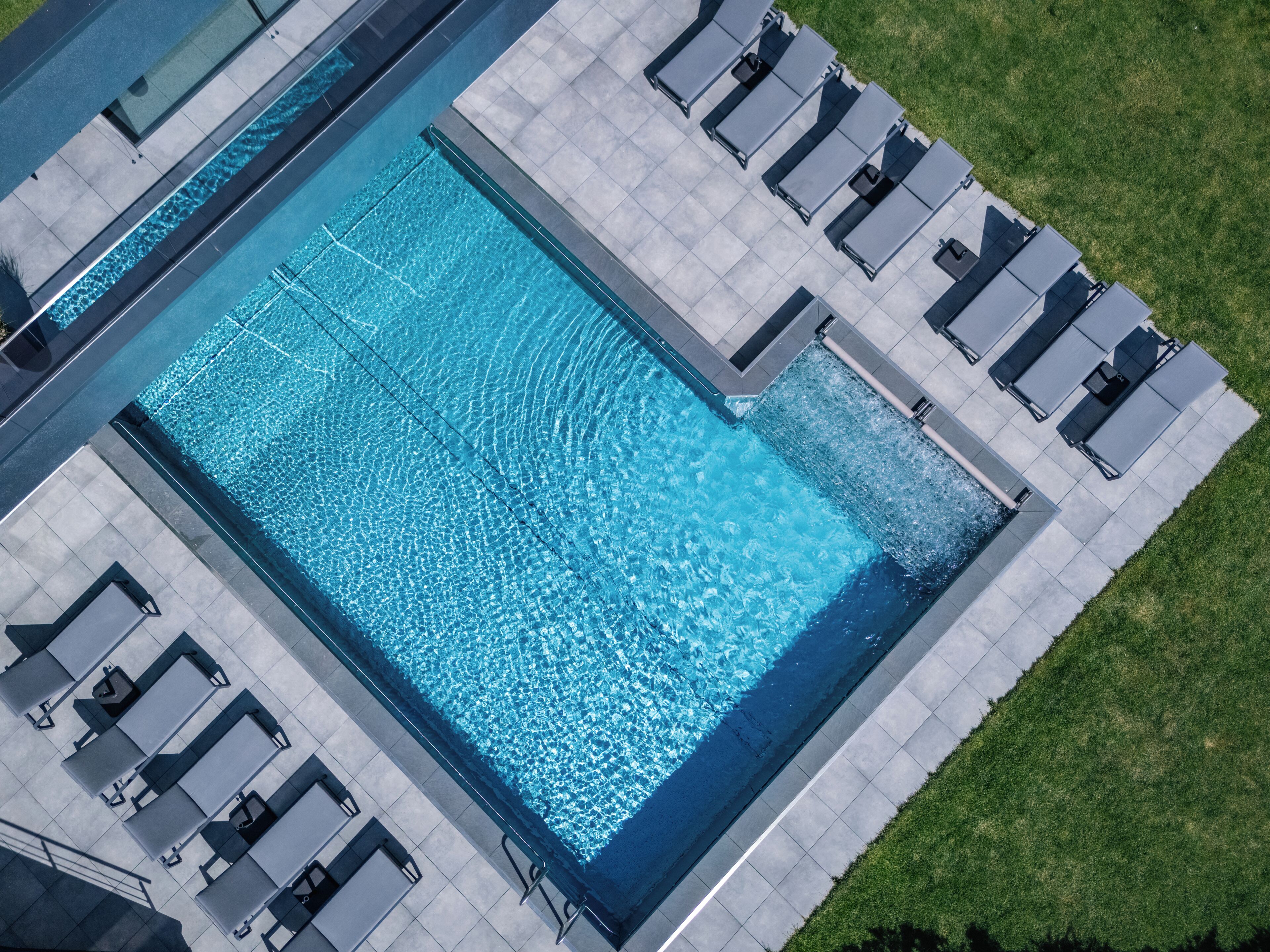 An aerial view of a rectangular swimming pool with a tiled deck surrounding it, equipped with multiple lounge chairs.