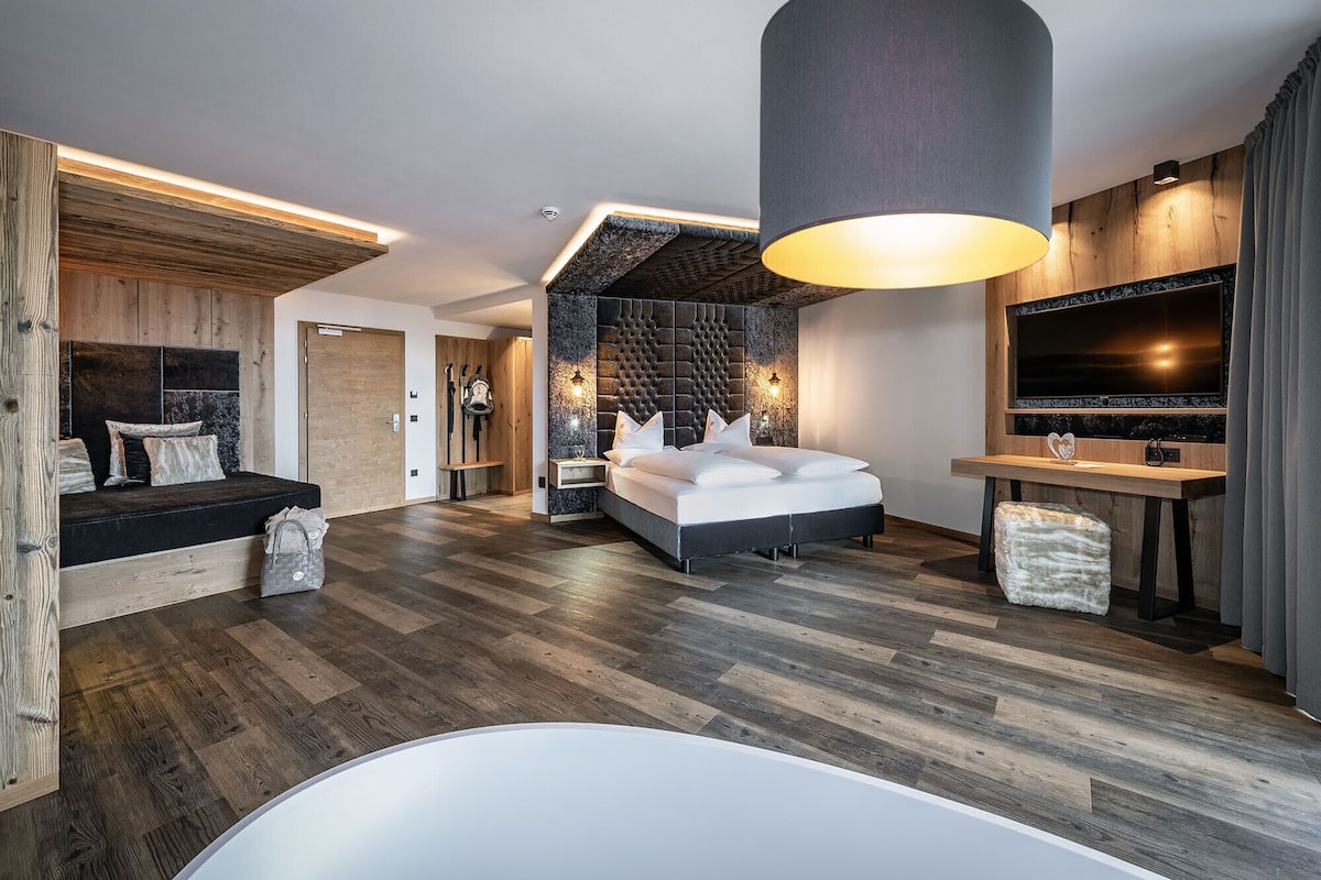 A modern hotel room with a large bed, a flat-screen TV, a wooden headboard, and a large window.