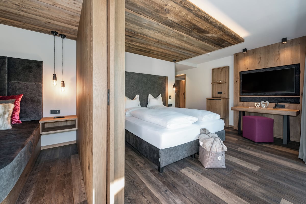 A modern bedroom with a large bed, wooden ceiling, built-in TV, and bedside tables.