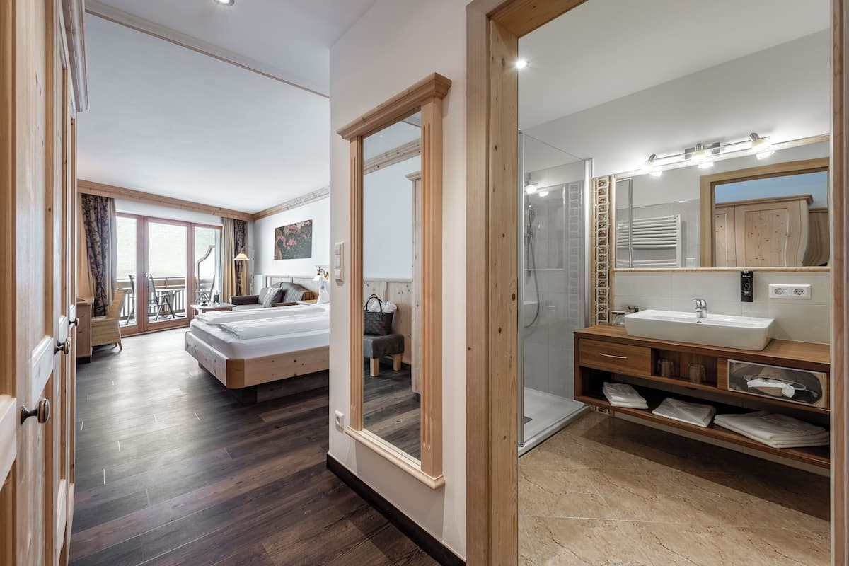 A modern hotel room with a large bed, a bathroom with a vanity and mirror, and a balcony with a view.