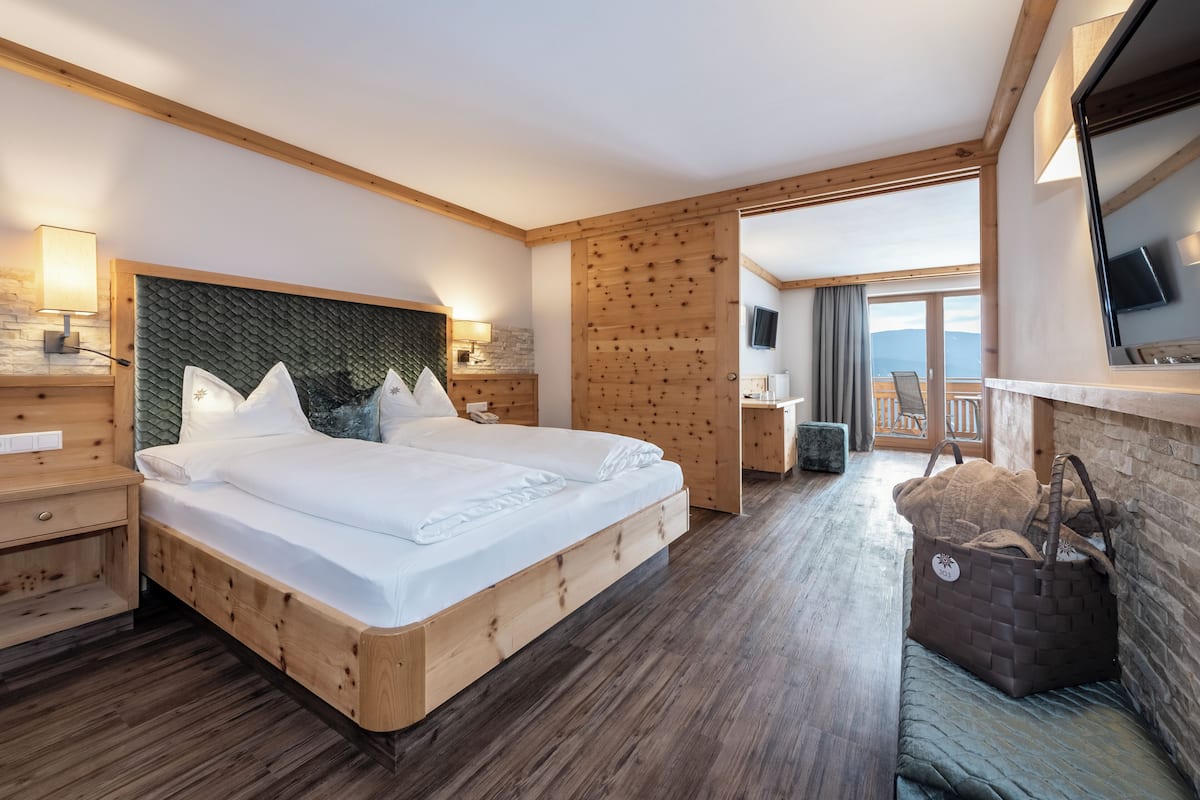A wooden-framed bedroom with a bed, bedside tables, a TV, and a view of the outdoors.