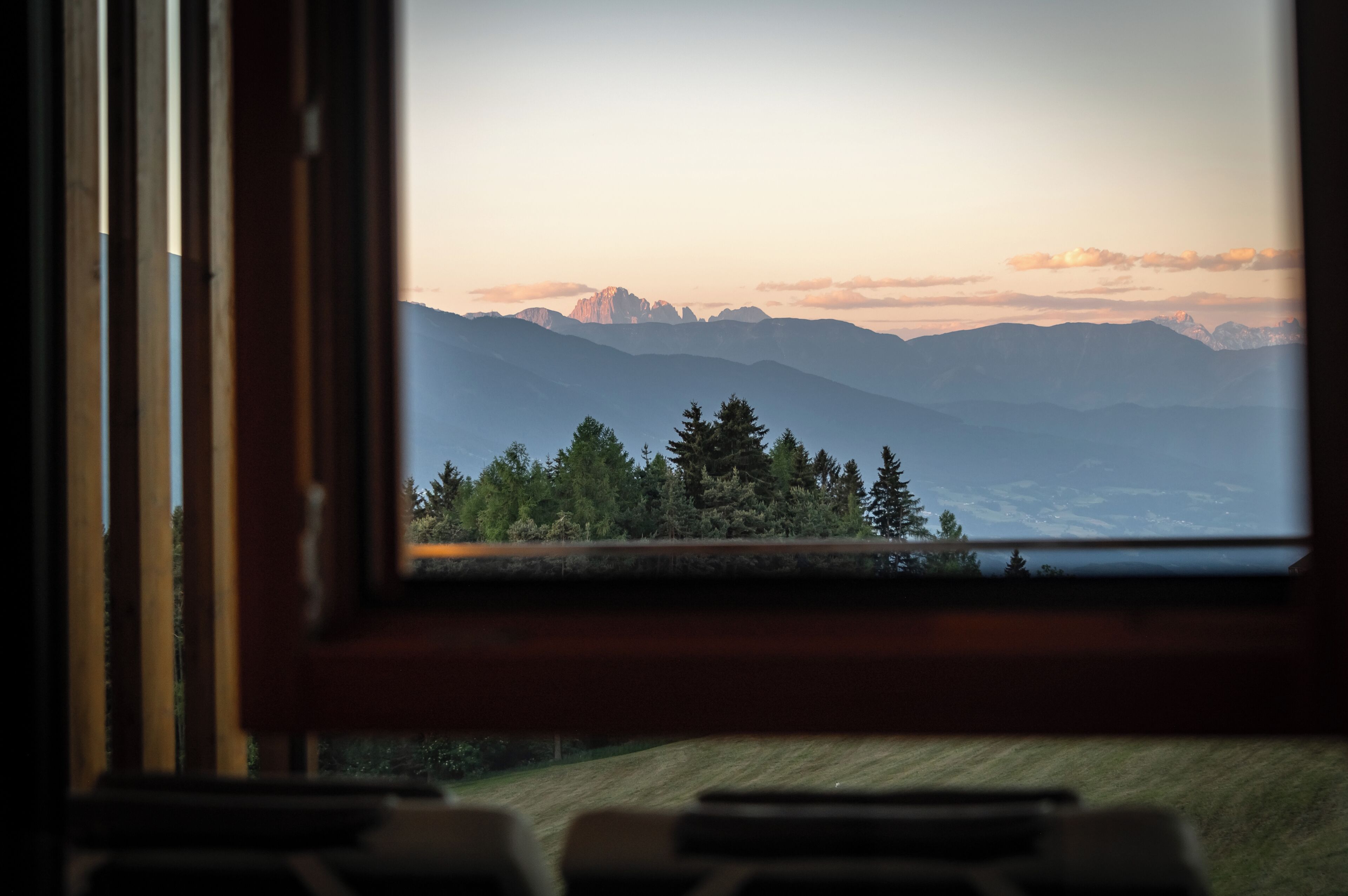 Une vue par la fenêtre sur un paysage montagneux, avec une zone boisée et des sommets lointains.