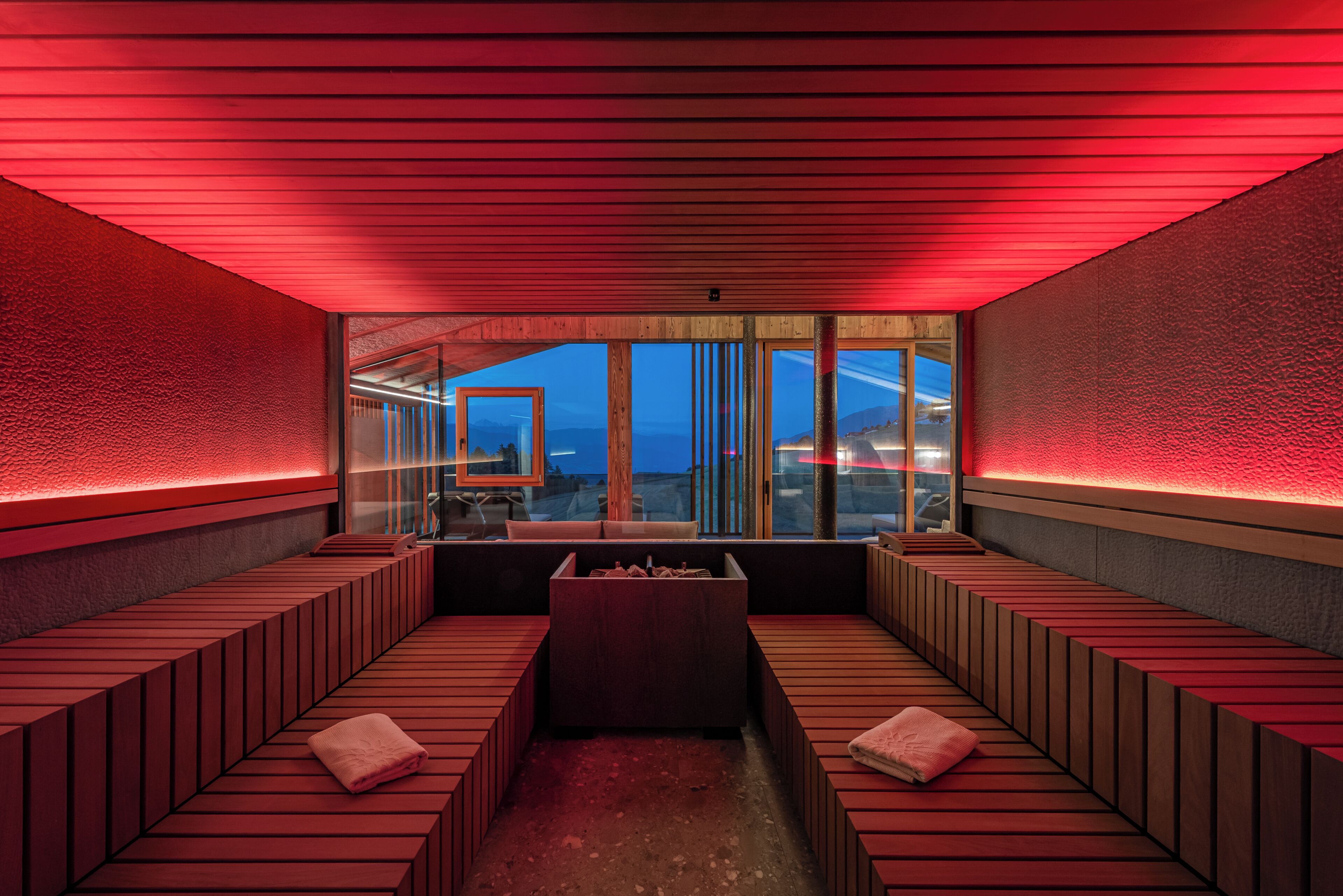 A modern spa room with wooden benches, a central seating area, and large windows offering a view.