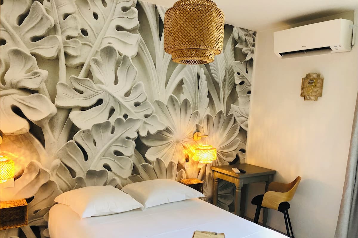 Een hotelkamer met een wand voorzien van een groot, gedetailleerd gesneden bladmotief, een bed met witte lakens, twee bedlampjes, een klein houten bureau en een stoel.