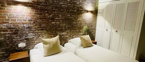 A room with two beds, a brick wall, a white wardrobe, and a small table.