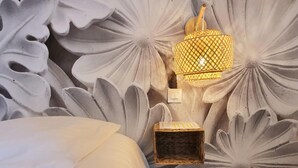 Une chambre avec un grand lit, un luminaire fixé au mur et un petit panier en osier.