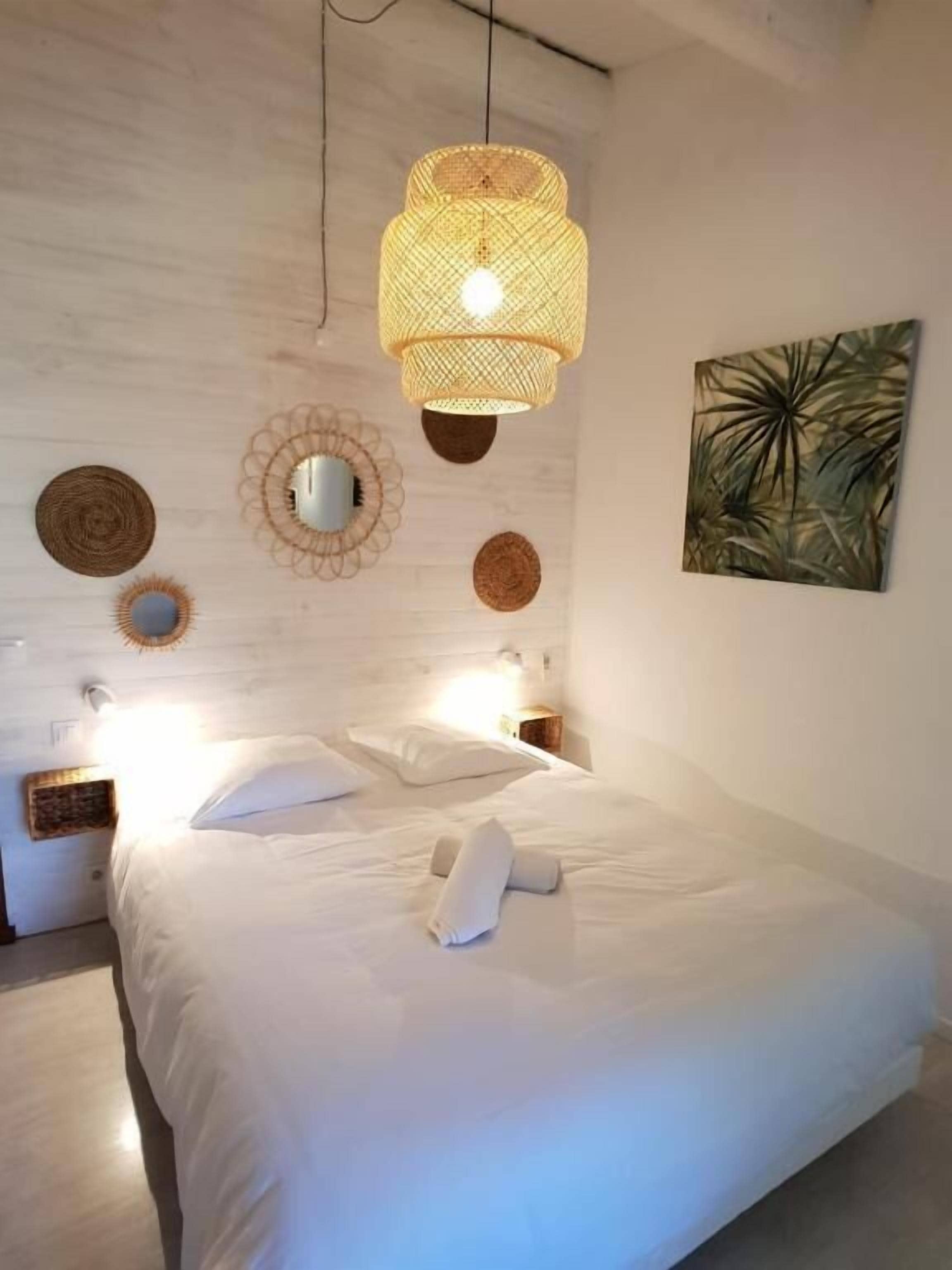A bedroom with a large bed, a hanging light fixture, a mirror, and a wall-mounted artwork.