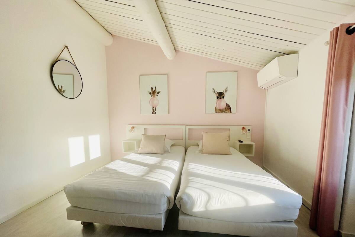 Een tweepersoonsbed met witte lakens, een nachtkastje met een lamp en een spiegel aan de muur.