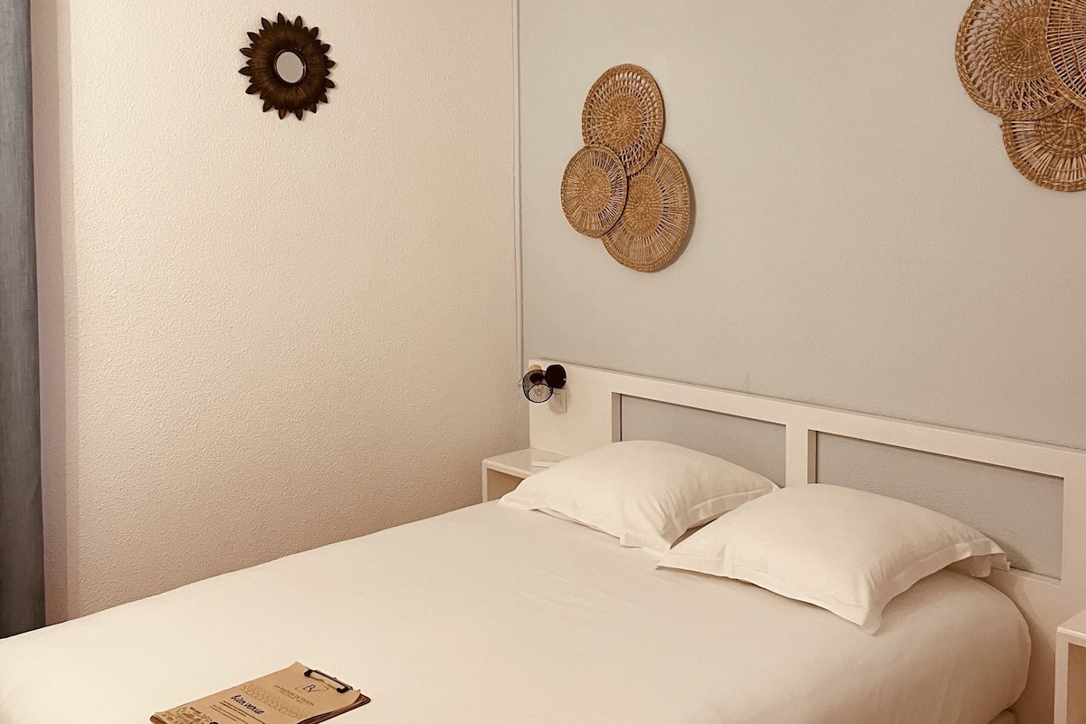 Een net opgemaakt bed met witte lakens, een plafondventilator en decoratieve muurkunst.