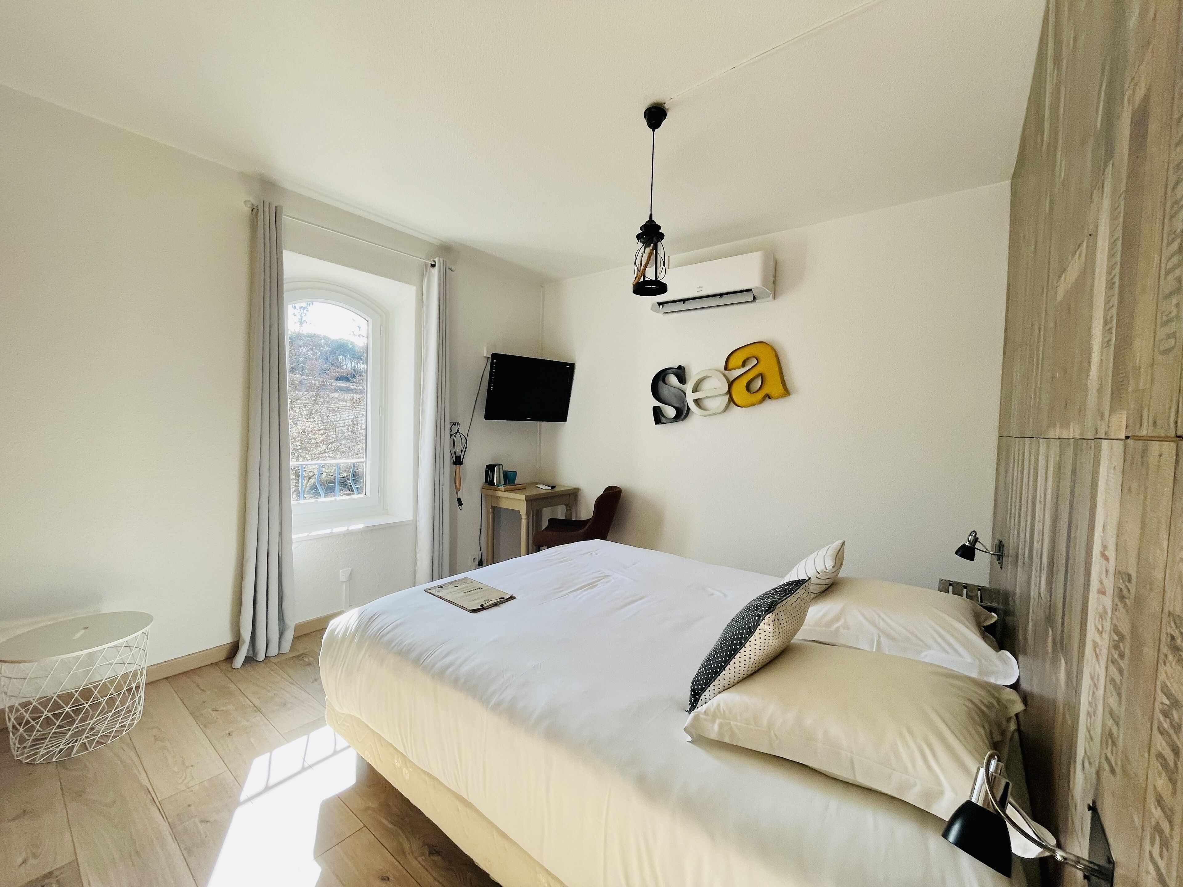 A bedroom with a bed, a desk, a TV, and a window with curtains.