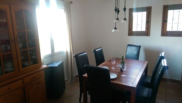 Un comedor con una mesa de madera, sillas negras y un aparador con puertas de cristal.