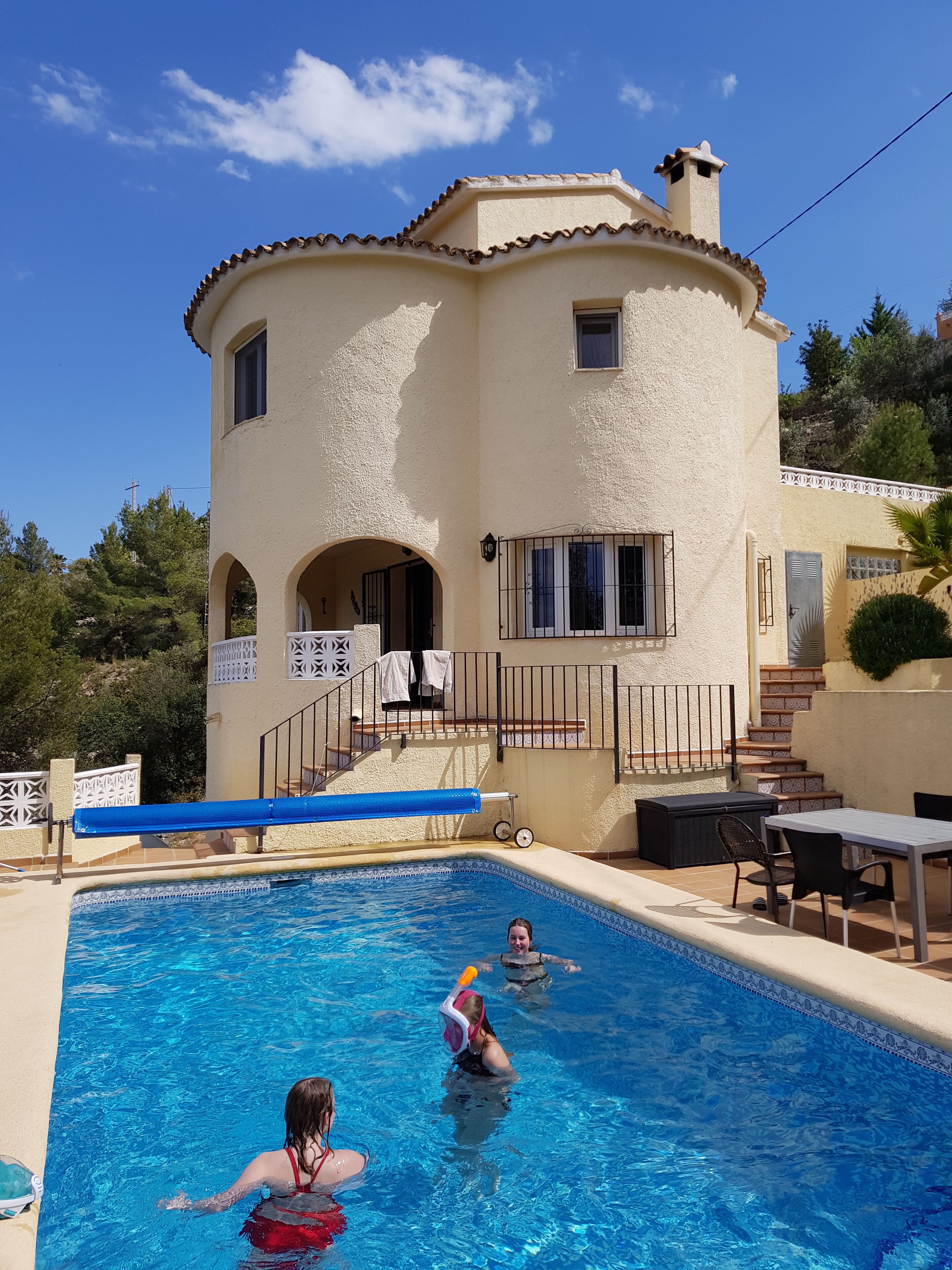 A pool area with a building in the background, a covered seating area, and a staircase leading to the building.