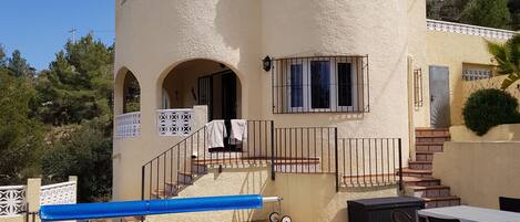 A pool area with a building in the background, a covered seating area, and a staircase leading to the building.