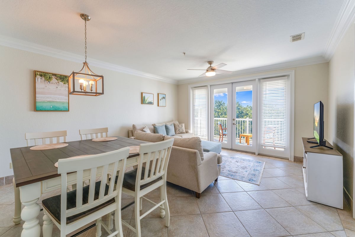 A dining area with a table and chairs, a sofa, a ceiling fan, and a television on a cabinet.