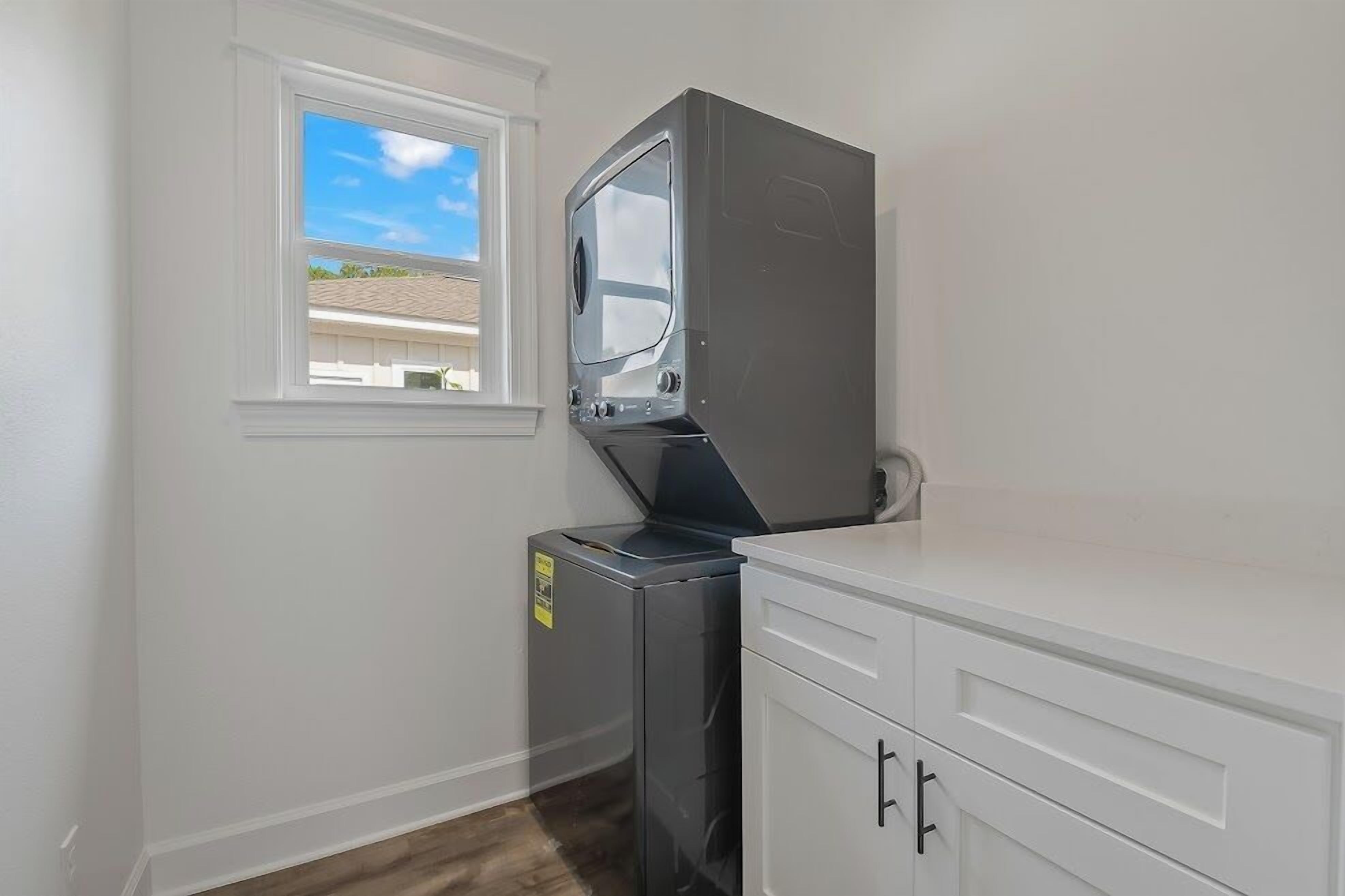 A laundry room with a washing machine, a dryer, and a window with a view of a house.