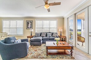 A living room with a sofa, armchair, coffee table, and a ceiling fan. - St James Bay Golf & Pickleball Resort (Carrabelle)