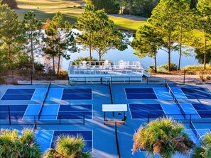 A tennis court area with a viewing deck overlooking a lake, surrounded by trees. - St James Bay Golf & Pickleball Resort (Carrabelle)