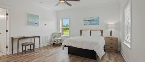 A bedroom with a bed, a desk, a chair, a ceiling fan, and a window.