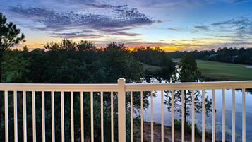 A wooden deck overlooking a lake with trees and a sunset in the background.