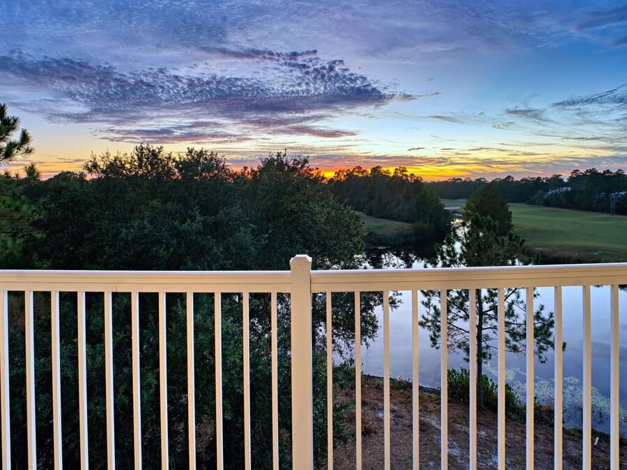 A wooden deck overlooking a lake with trees and a sunset in the background.