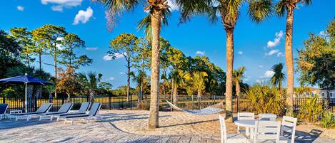 A wooden deck with lounge chairs and a table, surrounded by palm trees and a clear blue sky.