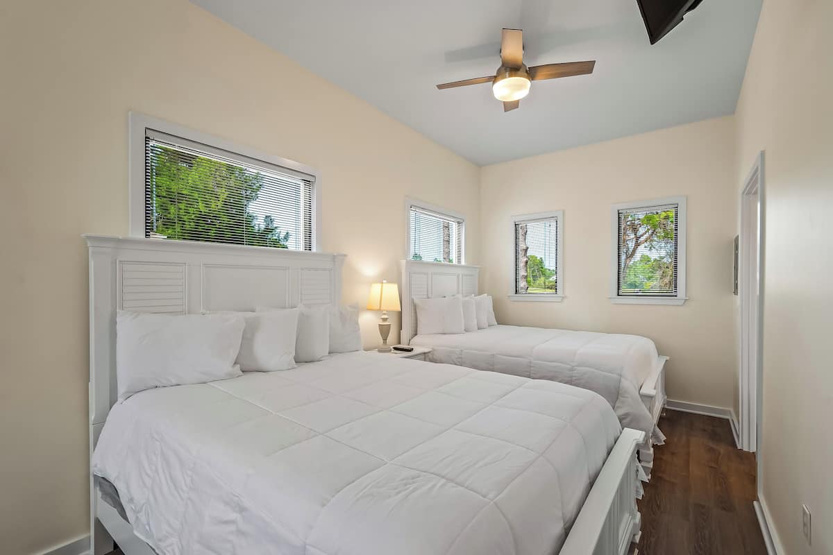 A bedroom with two beds, a ceiling fan, and windows with blinds.