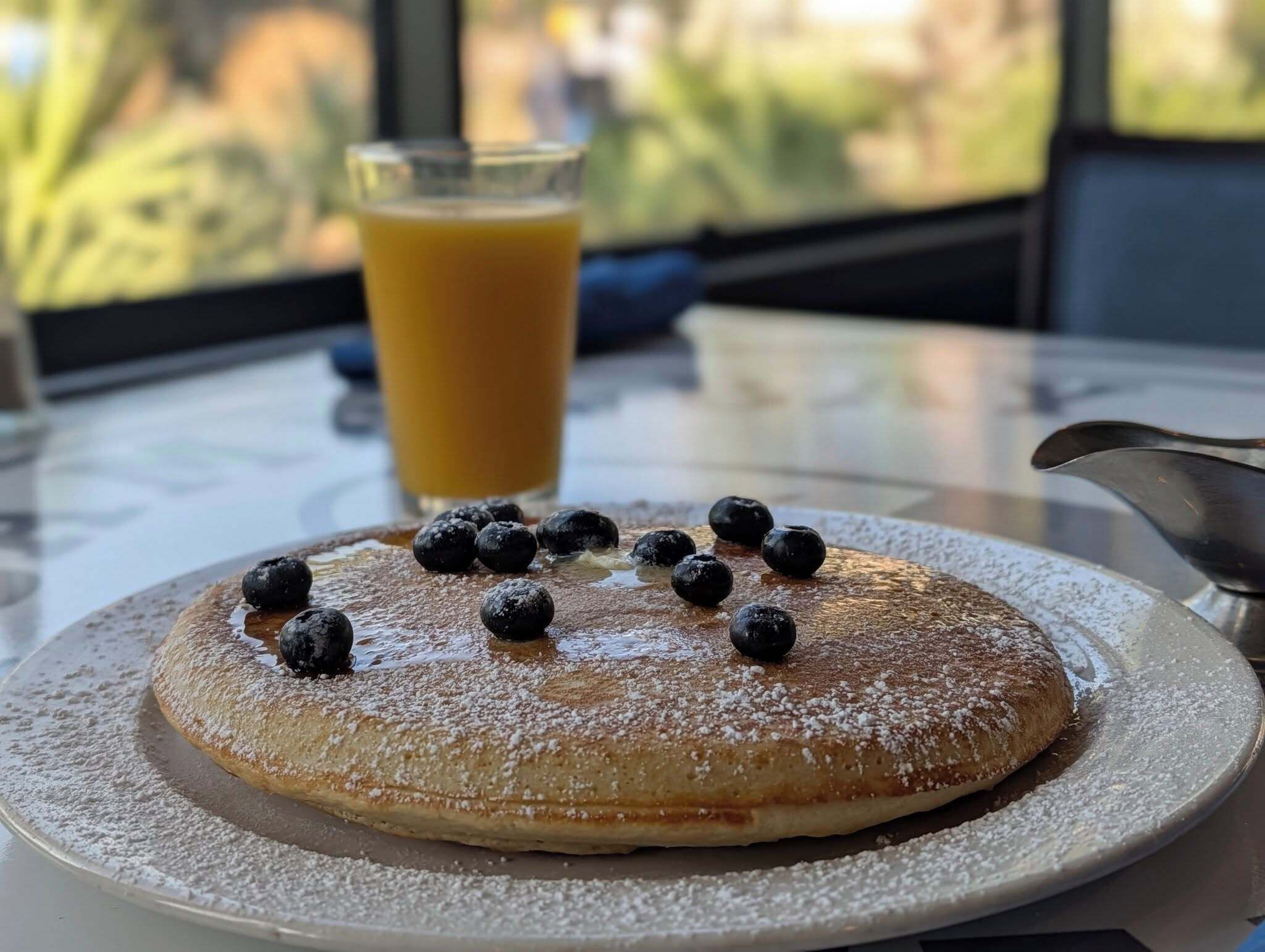 A breakfast plate with pancakes, blueberries, and a glass of orange juice on a table.