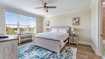 A bedroom with a bed, bedside tables, a ceiling fan, and large windows.