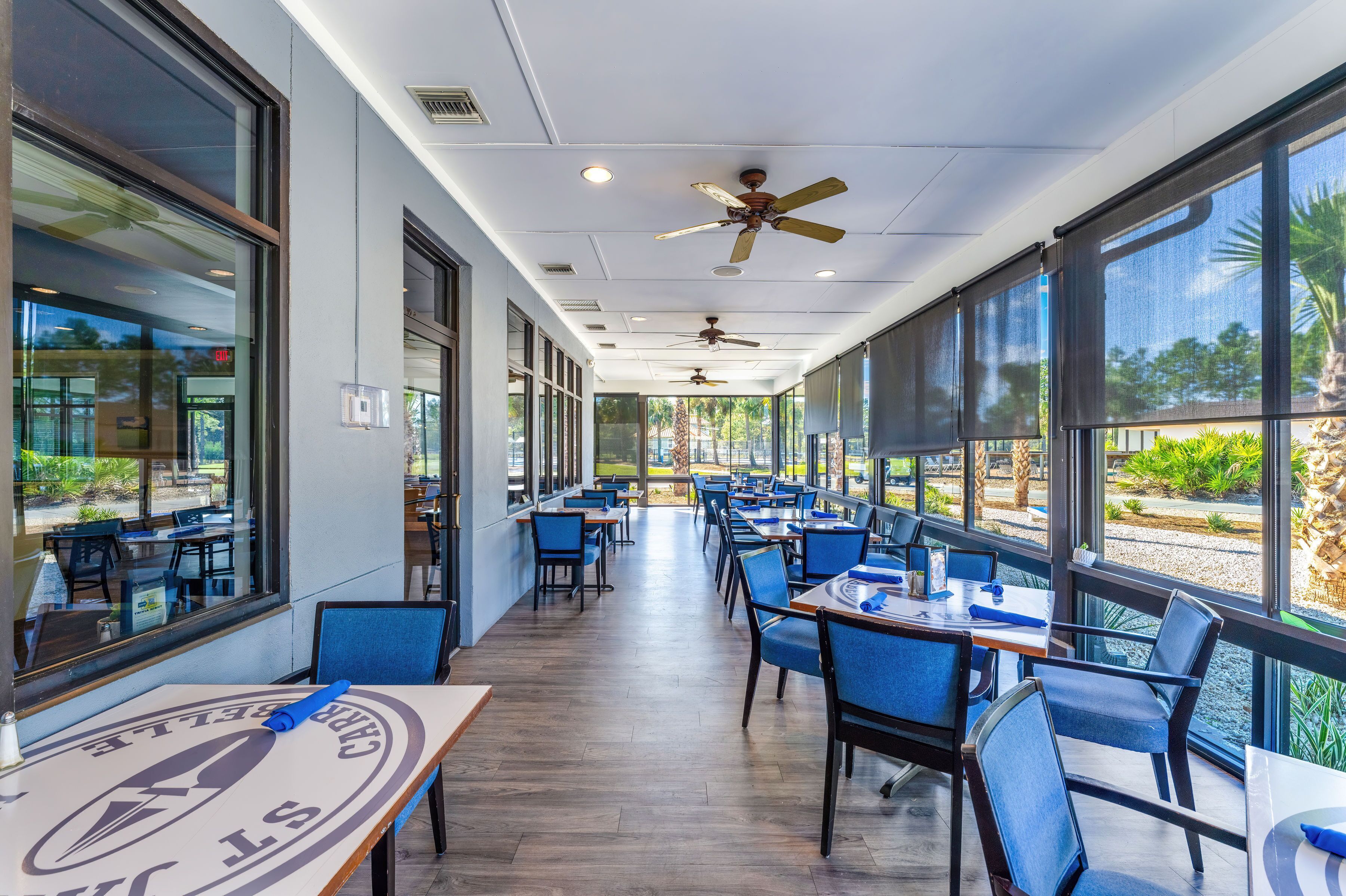 A restaurant with a long counter, blue chairs, and large windows offering a view of the outdoors.