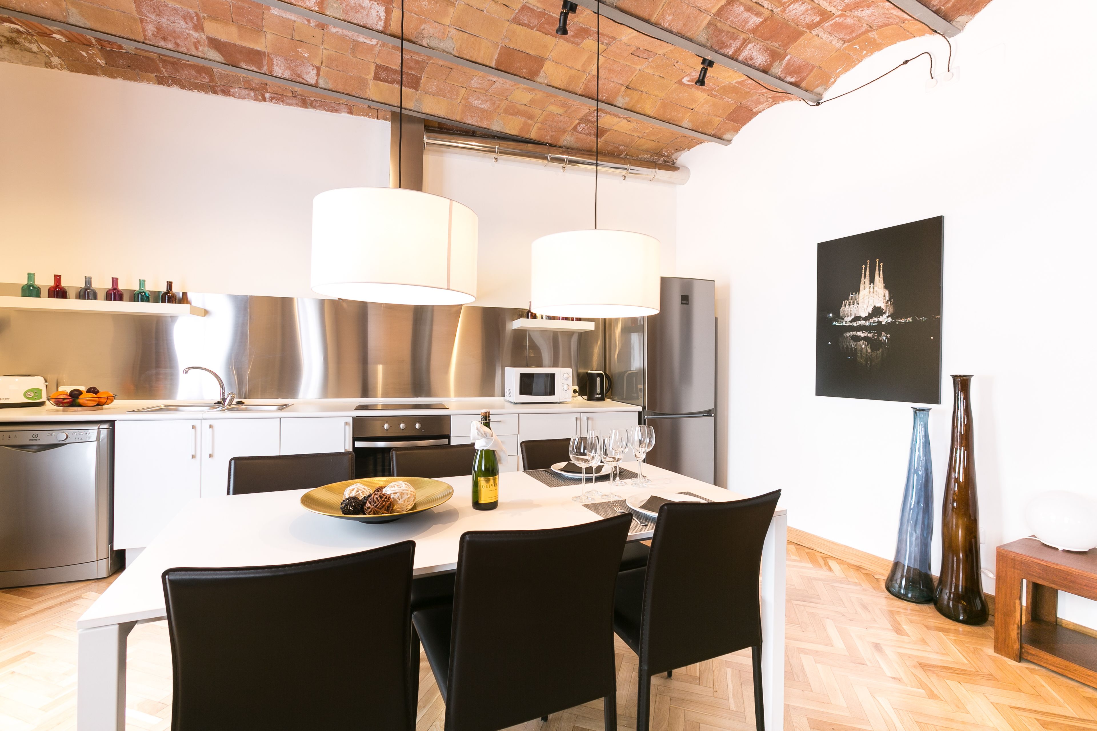 A modern kitchen with stainless steel appliances, a dining table set for four, and a large window overlooking the cityscape.