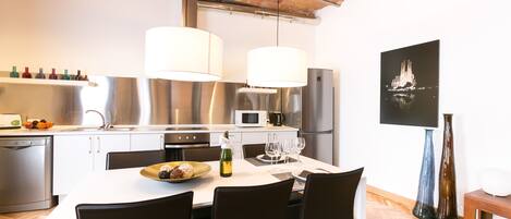 A modern kitchen with stainless steel appliances, a dining table set for four, and a large window overlooking the cityscape.
