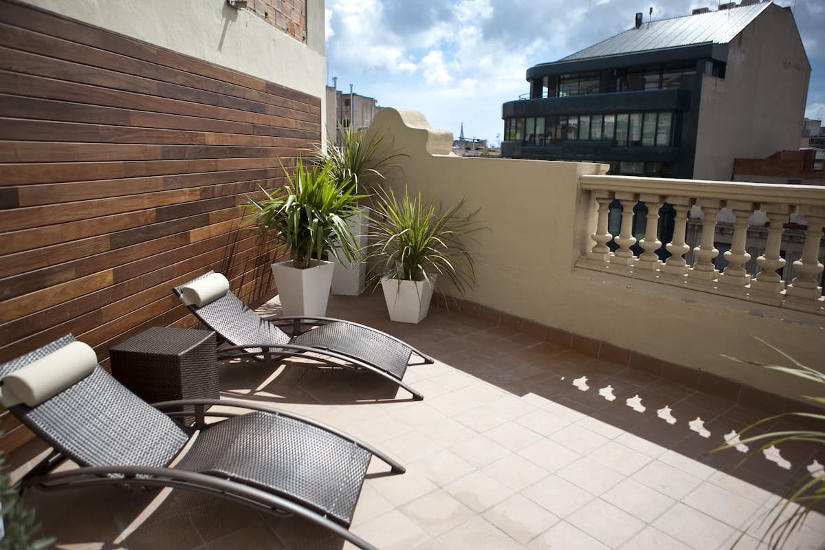 A rooftop terrace with two lounge chairs, potted plants, and a tiled floor.